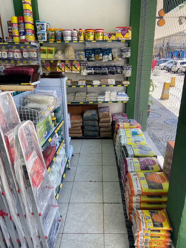 Cantinho da loja junto à entrada, com argamassas, rejuntes e ferragens organizados nas prateleiras