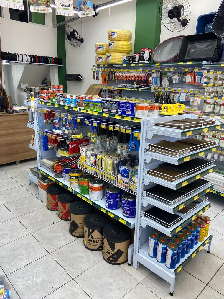 Seção de tintas, rolos, pincéis e espátulas, com lixas nas prateleiras inclinadas